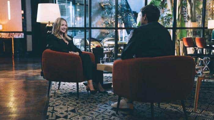 Un homme et une femme, Virginie Efira et HugoDécrypte, assis sur des chaises dans un hall d'entrée, en train de filmer "L'interview face cachée.