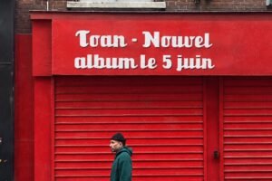 Toan, rappeur et psychologue, devant une enseigne rouge annonçant son nouvel album Le Soleil de Midi le 5 juin