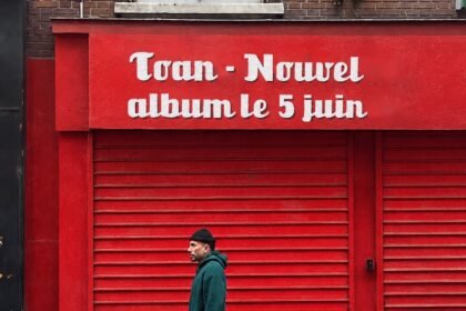 Toan, rappeur et psychologue, devant une enseigne rouge annonçant son nouvel album Le Soleil de Midi le 5 juin