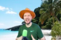 Unchained avec chapeau orange devant un décor de plage tropicale, micro vert à la main