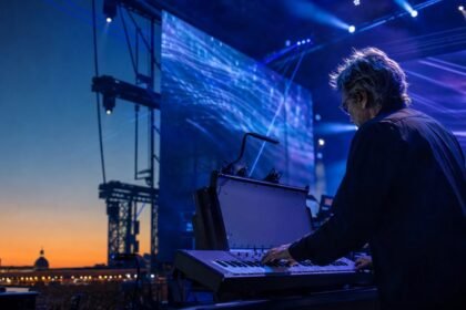 Jean-Michel Jarre jouant des synthétiseurs sur une scène en plein air, éclairée de bleu et de violet