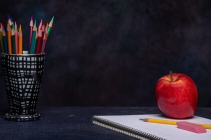 Crayons de couleur dans un pot, gomme et cahier posés sur une table, avec une pomme rouge