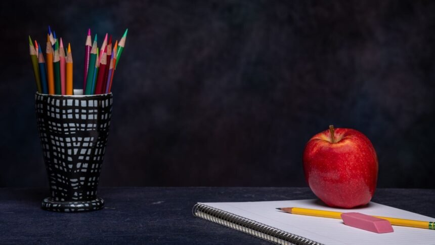 Crayons de couleur dans un pot, gomme et cahier posés sur une table, avec une pomme rouge