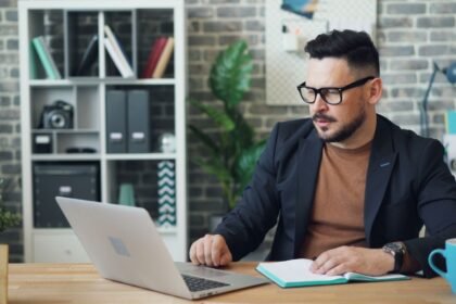 Un homme en lunettes travaille sur un ordinateur portable dans un bureau avec des plantes et des étagères