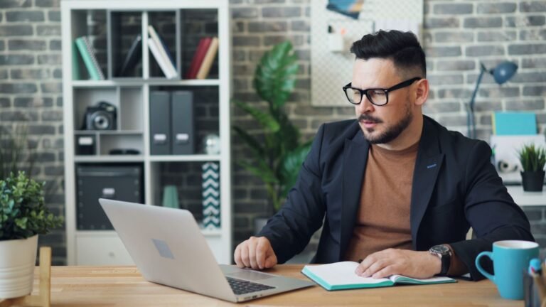 Un homme en lunettes travaille sur un ordinateur portable dans un bureau avec des plantes et des étagères