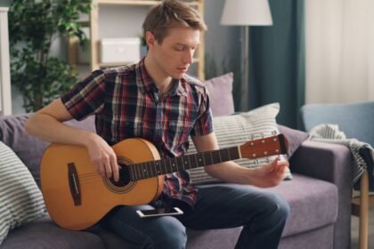 Jeune homme jouant de la guitare acoustique sur un canapé