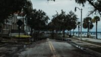 Vigilance rouge haute-corse levée à 19 h 17 : rester chez soi jusqu'à minuit Rue urbaine inondée avec palmiers sous un ciel chargé, illustration de la vigilance rouge en Haute-Corse