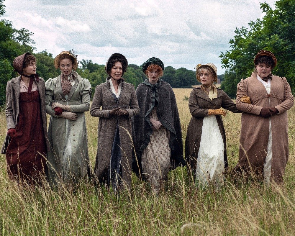Six femmes en tenues d’époque et bonnets marchent côte à côte dans un champ