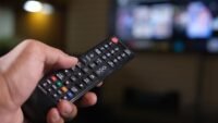 Personne tenant une télécommande devant un écran de télévision flou