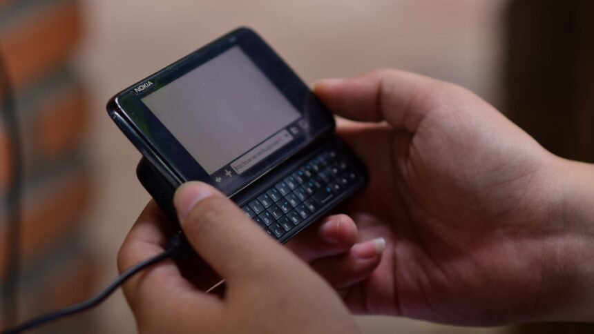 2g coupée chez orange le 6 octobre : 1,22 million de sim, vérifiez votre mobile Mains tenant un ancien téléphone portable à clavier, de type 2G